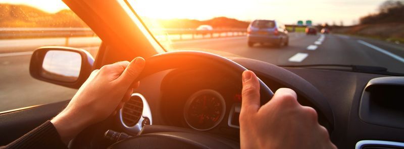 Safety - Photo of drivers hand on steering wheel with amber glow of sun creating lens flare.